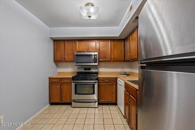 kitchen featuring brown cabinetry, light countertops, stainless steel appliances, and light tile patterned flooring