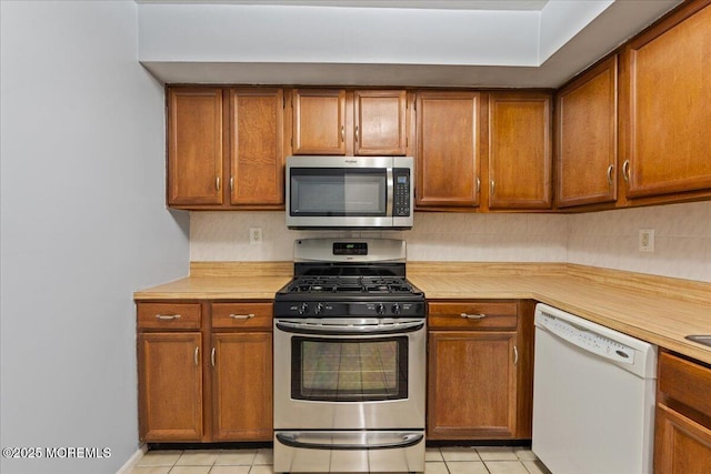 kitchen featuring light countertops, appliances with stainless steel finishes, brown cabinetry, and light tile patterned floors