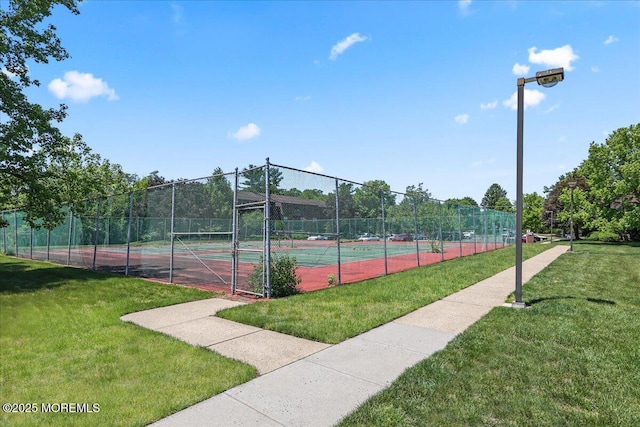 view of tennis court featuring fence and a lawn
