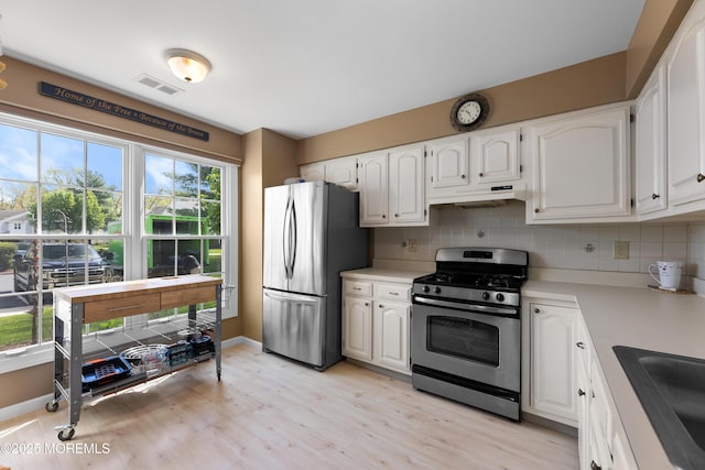 kitchen with white cabinets, appliances with stainless steel finishes, a sink, under cabinet range hood, and visible vents