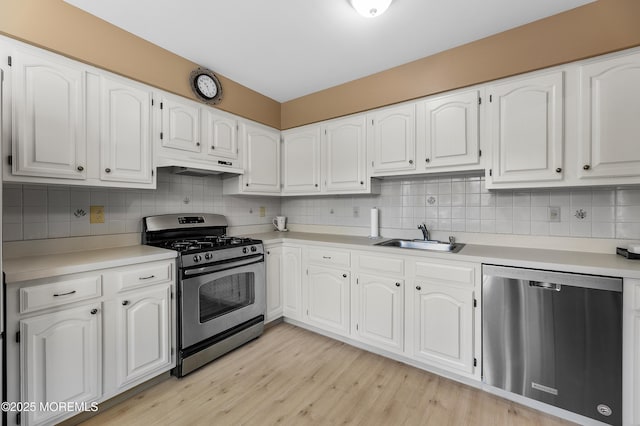 kitchen with appliances with stainless steel finishes, a sink, white cabinets, under cabinet range hood, and light wood-style flooring