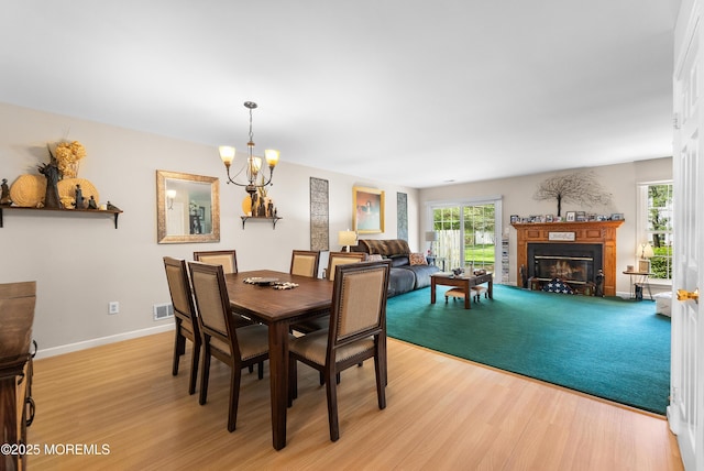 dining room featuring an inviting chandelier, visible vents, a glass covered fireplace, baseboards, and light wood finished floors