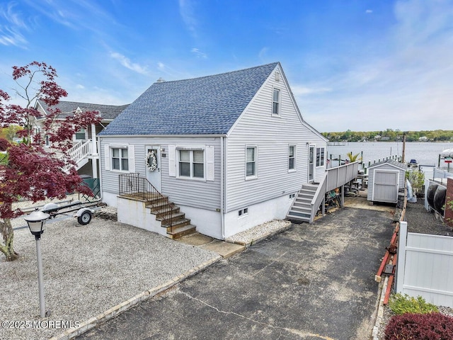 view of front of home with roof with shingles, fence, stairs, a storage shed, and an outdoor structure