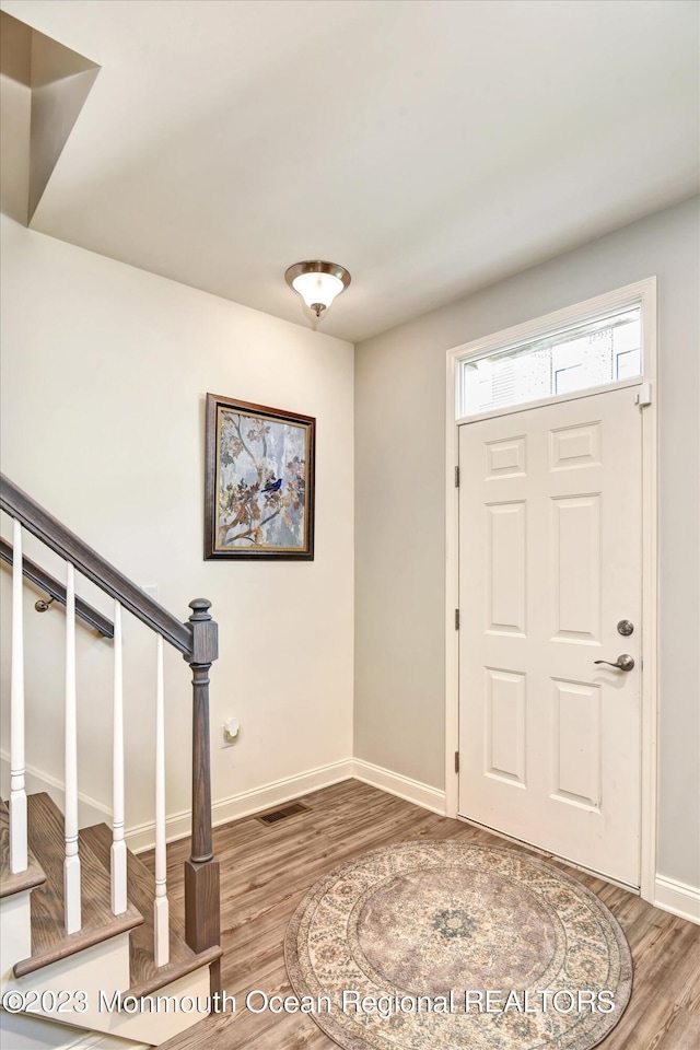 foyer entrance with baseboards, stairs, wood finished floors, and visible vents
