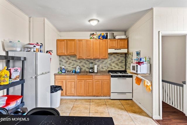 kitchen featuring white appliances, under cabinet range hood, tasteful backsplash, light tile patterned floors, and stone counters