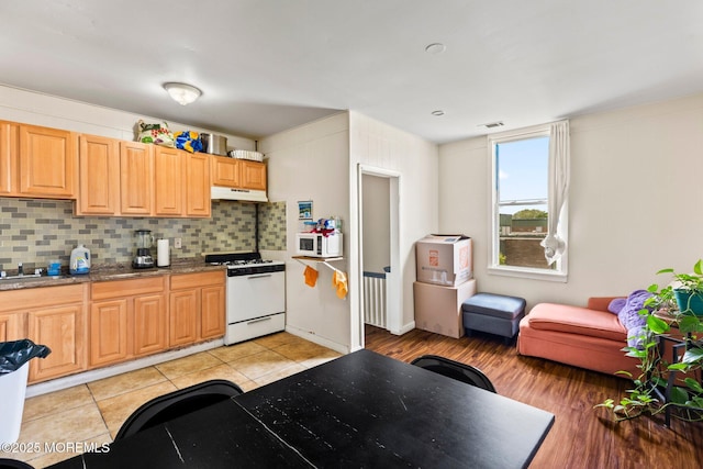 kitchen featuring white appliances, decorative backsplash, under cabinet range hood, and light brown cabinetry