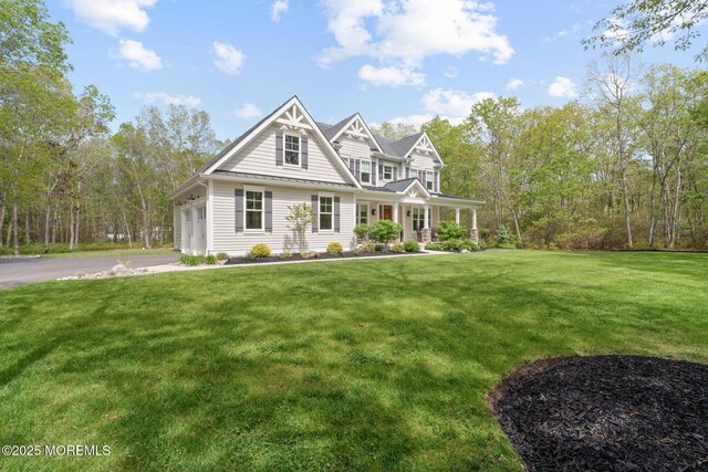 view of front of property featuring covered porch, a front lawn, a garage, and a standing seam roof