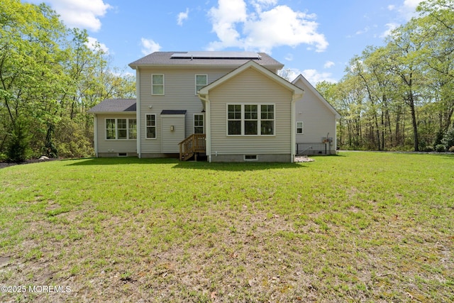 back of property with roof mounted solar panels and a lawn