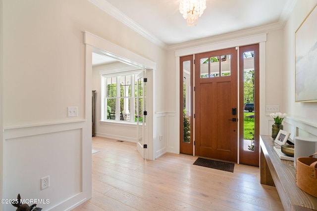 entryway featuring a decorative wall, light wood finished floors, ornamental molding, a chandelier, and a wainscoted wall