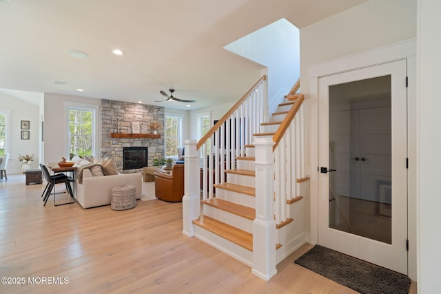 stairway with wood finished floors, ceiling fan, a stone fireplace, recessed lighting, and baseboards