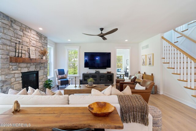 living area featuring light wood-style flooring, stairs, ceiling fan, a stone fireplace, and recessed lighting
