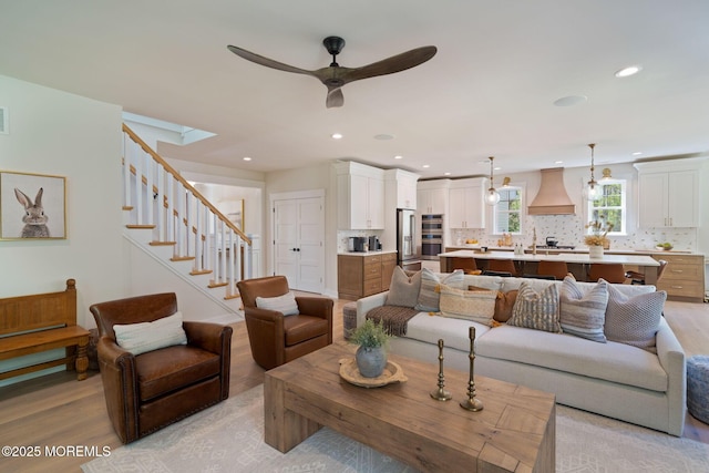 living room with light wood-type flooring, ceiling fan, recessed lighting, and stairway
