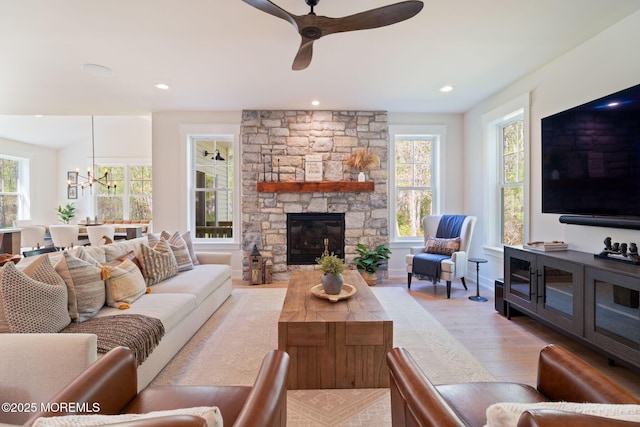 living room featuring light wood-style flooring, ceiling fan, a chandelier, a stone fireplace, and recessed lighting
