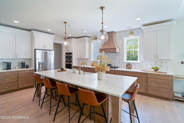 kitchen with custom exhaust hood, appliances with stainless steel finishes, tasteful backsplash, a kitchen bar, and an island with sink
