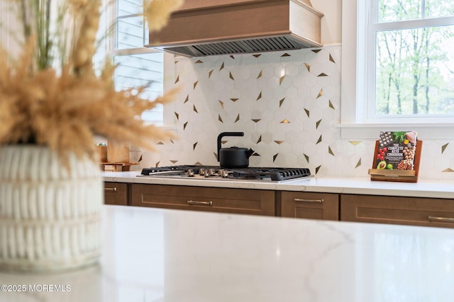 kitchen featuring decorative backsplash, stainless steel gas stovetop, premium range hood, and light countertops