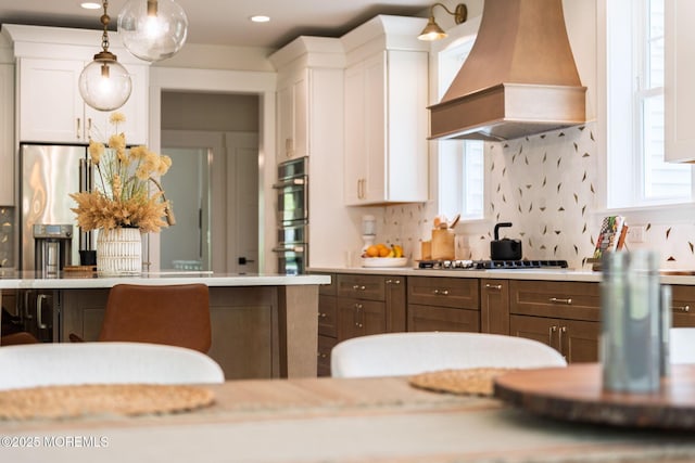 kitchen featuring premium range hood, gas stovetop, white cabinets, light countertops, and decorative light fixtures
