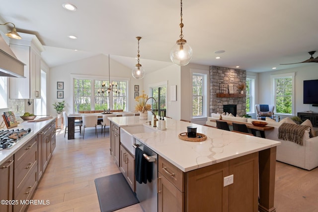 kitchen with appliances with stainless steel finishes, a sink, a stone fireplace, light wood-style floors, and open floor plan
