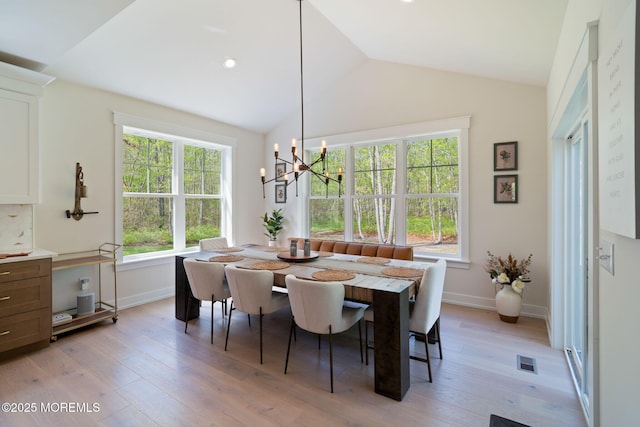 dining space with healthy amount of natural light, lofted ceiling, light wood-style floors, a chandelier, and baseboards