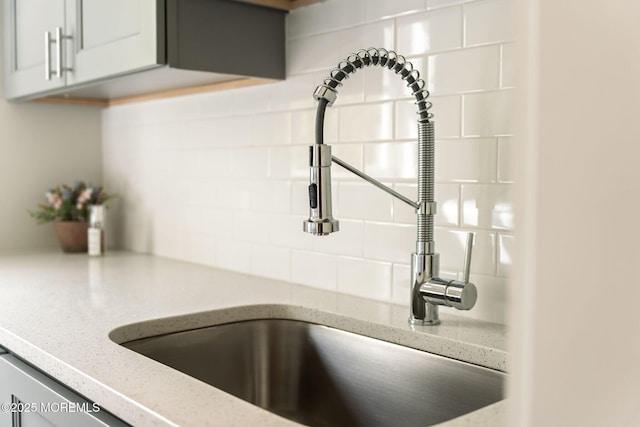 kitchen view of a sink, decorative backsplash, and light stone counters