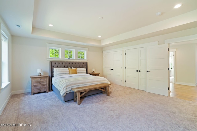 bedroom featuring two closets, light colored carpet, recessed lighting, baseboards, and a raised ceiling
