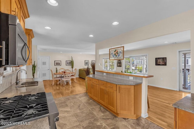 kitchen with appliances with stainless steel finishes, stone counters, a sink, and a healthy amount of sunlight