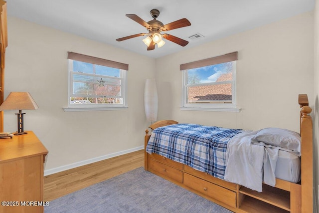 bedroom featuring visible vents, baseboards, wood finished floors, and multiple windows