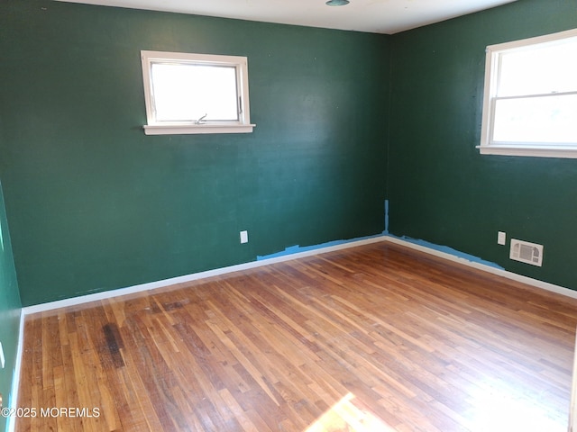 unfurnished room featuring visible vents, wood finished floors, and a wealth of natural light