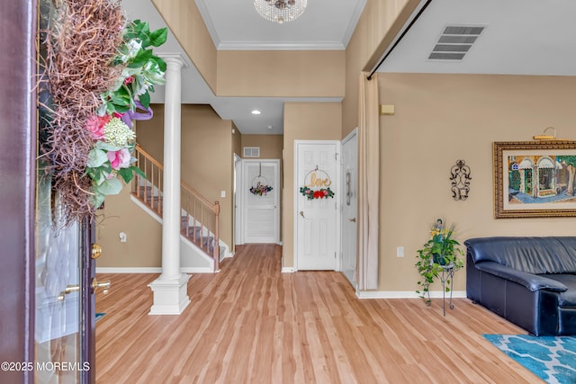 foyer featuring baseboards, wood finished floors, stairway, ornate columns, and crown molding