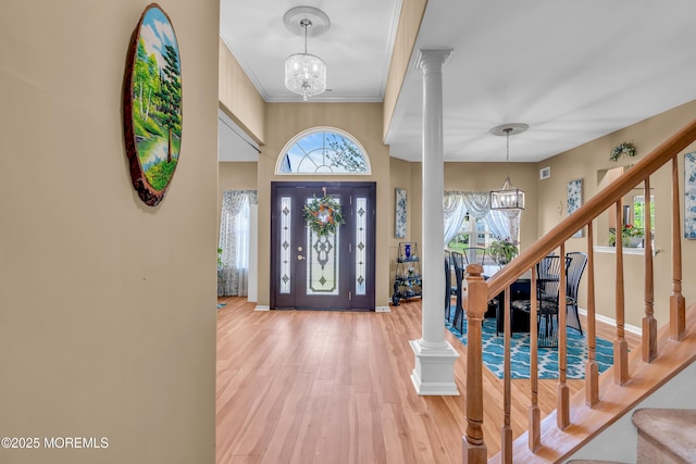entryway featuring a chandelier, wood finished floors, ornate columns, stairs, and crown molding