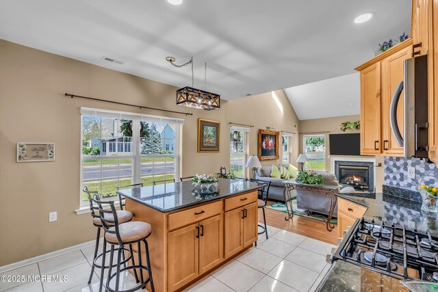 kitchen featuring stainless steel microwave, light tile patterned floors, healthy amount of natural light, a kitchen breakfast bar, and lofted ceiling