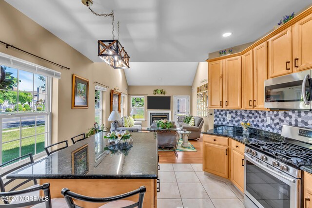 kitchen with appliances with stainless steel finishes, vaulted ceiling, plenty of natural light, open floor plan, and light tile patterned floors