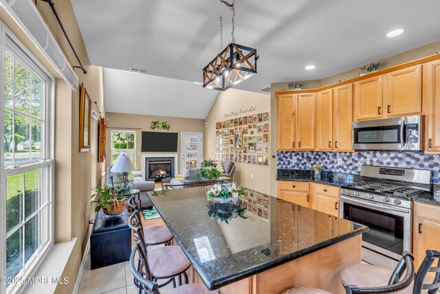 kitchen featuring stainless steel appliances, light brown cabinets, lofted ceiling, a glass covered fireplace, and a breakfast bar area