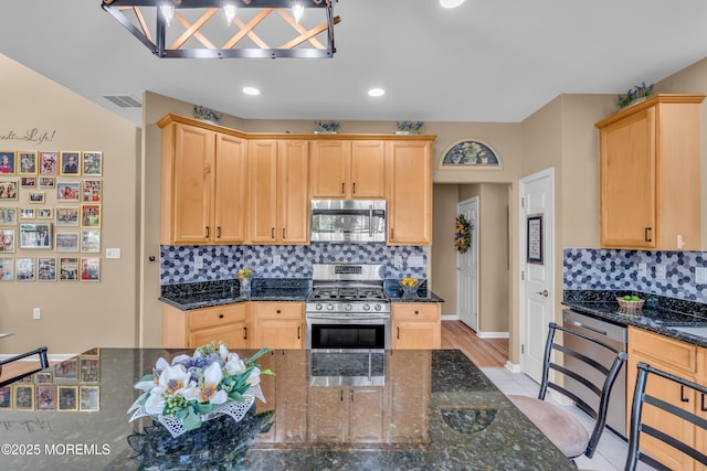 kitchen featuring appliances with stainless steel finishes, light brown cabinets, decorative backsplash, baseboards, and dark stone countertops