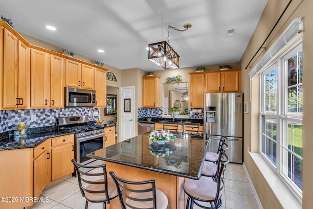 kitchen with stainless steel appliances, a kitchen bar, tasteful backsplash, light tile patterned flooring, and a center island with sink