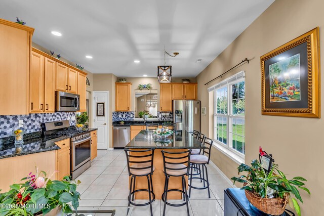kitchen featuring appliances with stainless steel finishes, tasteful backsplash, a kitchen breakfast bar, light tile patterned floors, and a center island