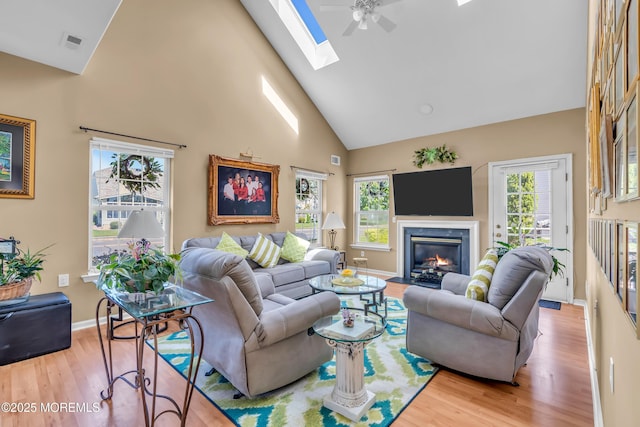 living room featuring high vaulted ceiling, wood finished floors, plenty of natural light, a skylight, and a fireplace