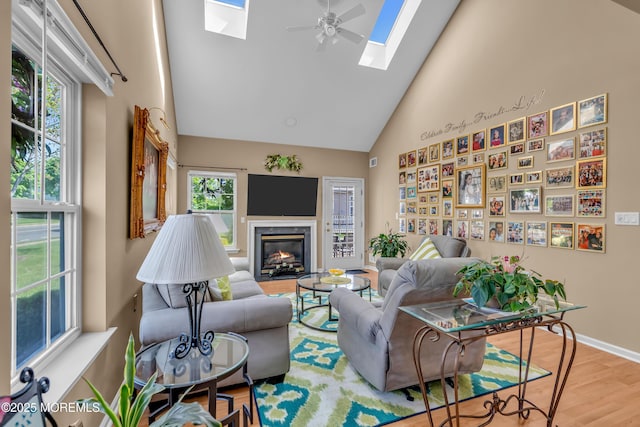 living room featuring a skylight, high vaulted ceiling, wood finished floors, a fireplace, and baseboards