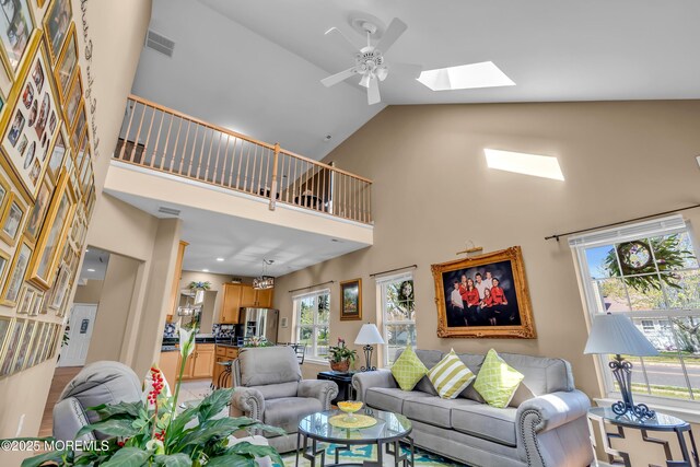 living room featuring a skylight, high vaulted ceiling, and a ceiling fan