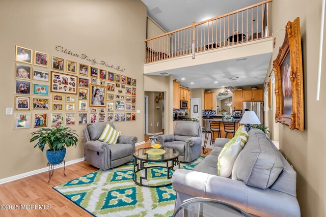 living area featuring light wood finished floors, baseboards, and a high ceiling
