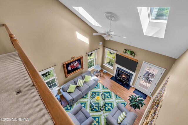 living room with a skylight, high vaulted ceiling, a glass covered fireplace, healthy amount of natural light, and wood finished floors