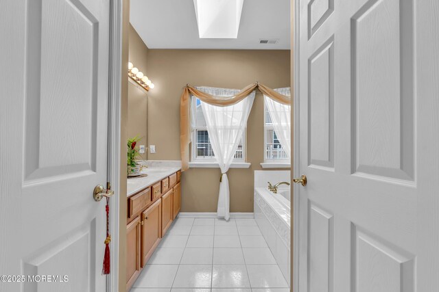 bathroom featuring a skylight, vanity, tile patterned flooring, a garden tub, and baseboards