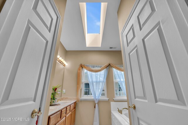 bathroom with vanity, a garden tub, and a skylight