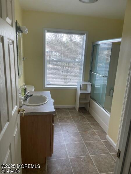 bathroom with bath / shower combo with glass door, baseboards, and vanity