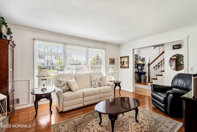 living room featuring crown molding, visible vents, wood finished floors, and stairway