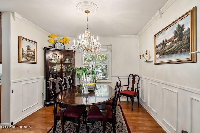 dining room featuring crown molding, a decorative wall, a chandelier, and wood finished floors