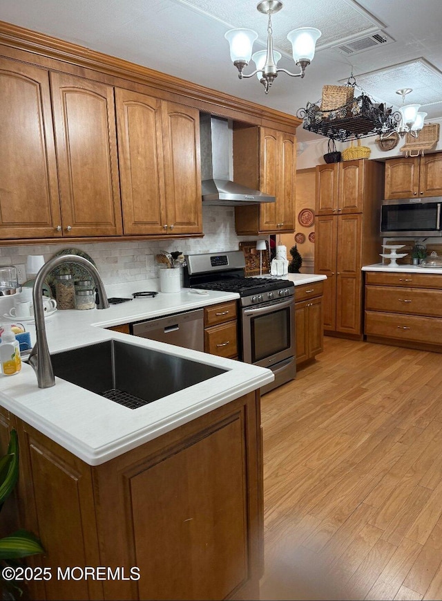 kitchen featuring wall chimney range hood, stainless steel appliances, a notable chandelier, and a sink