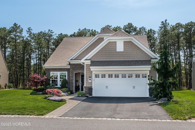 craftsman-style home with a garage, stone siding, a front yard, a shingled roof, and driveway