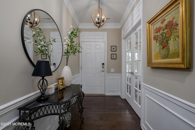 foyer with crown molding, dark wood-style floors, a wainscoted wall, a chandelier, and french doors