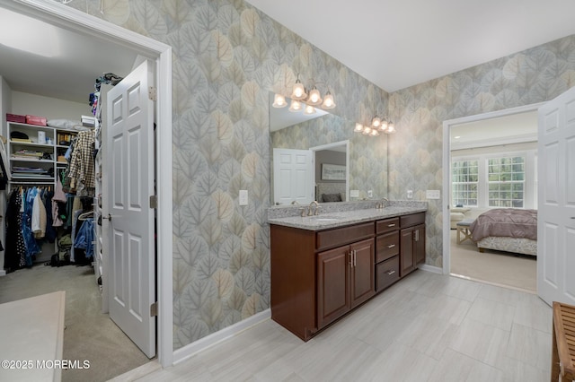 bathroom featuring double vanity, a walk in closet, a sink, and connected bathroom