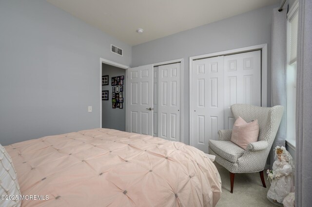 bedroom featuring visible vents, carpet, and two closets